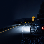Night driving on a winding mountain road with headlights illuminating the road and a visible speedometer.