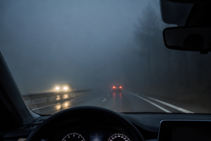 View from inside a car on a foggy road at night with headlights ahead