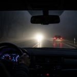 View from inside a car driving at night on a foggy road with headlights and taillights visible.