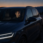 Man driving a modern black SUV on a scenic mountain road at dusk
