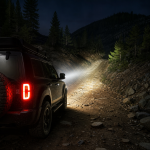Off-road SUV with headlights illuminating a rugged mountain trail at night