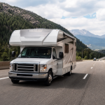 White motorhome driving on a scenic mountain highway under a partly cloudy sky