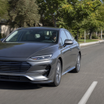 Gray modern sedan driving on a suburban road with trees and other cars in the background