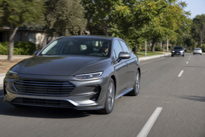 Gray modern sedan driving on a suburban road with trees and other cars in the background