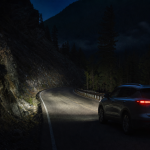 SUV headlights illuminate a winding mountain road at night.