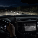 Dashboard display and rearview camera view on a dark road at night